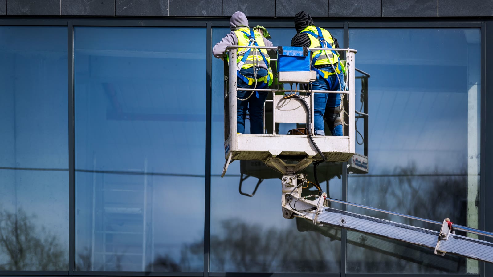 To personer pudser vinduer fra en lift på en bygning